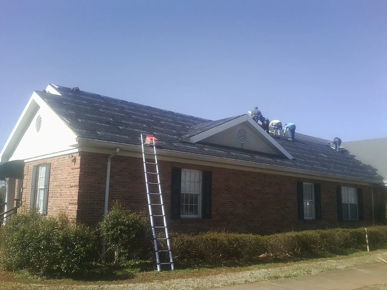 Crew tearing shingles off a brick ranch roof with a ladder set — Metal Roof Repair work by our crew in Clarksboro
