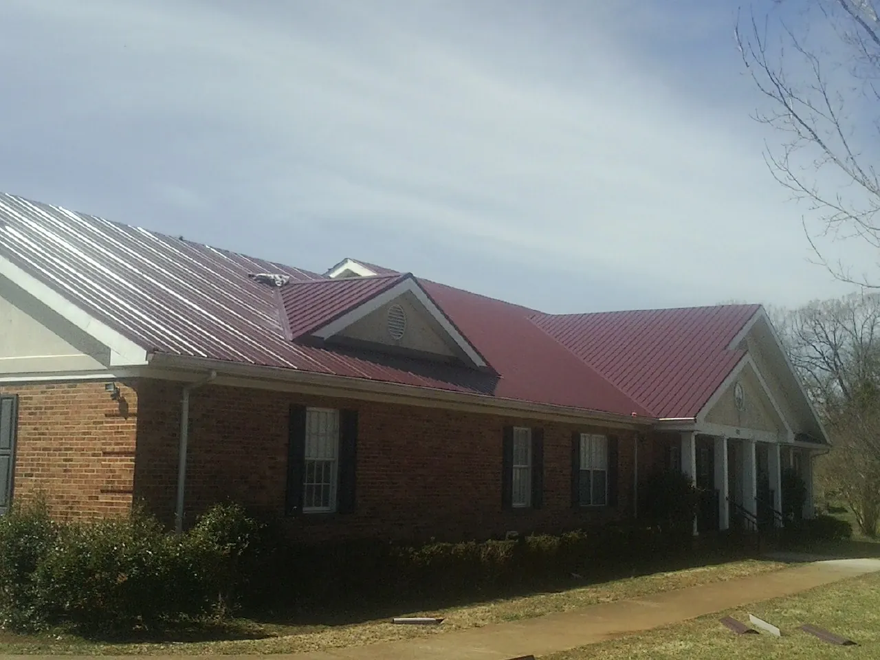Red metal roof with gabled entries on a long brick building, from a Hail Damage Roof Repair job in Clarksboro