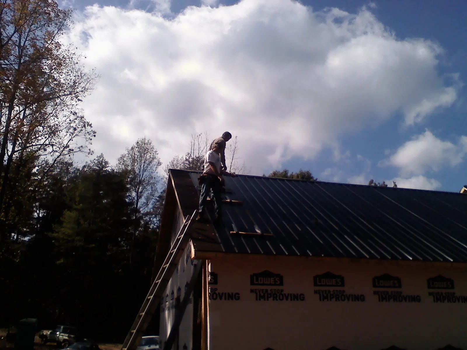 Roofer fastening dark metal panels high against a cloudy sky, from a Roof Inspection job in Clarksboro