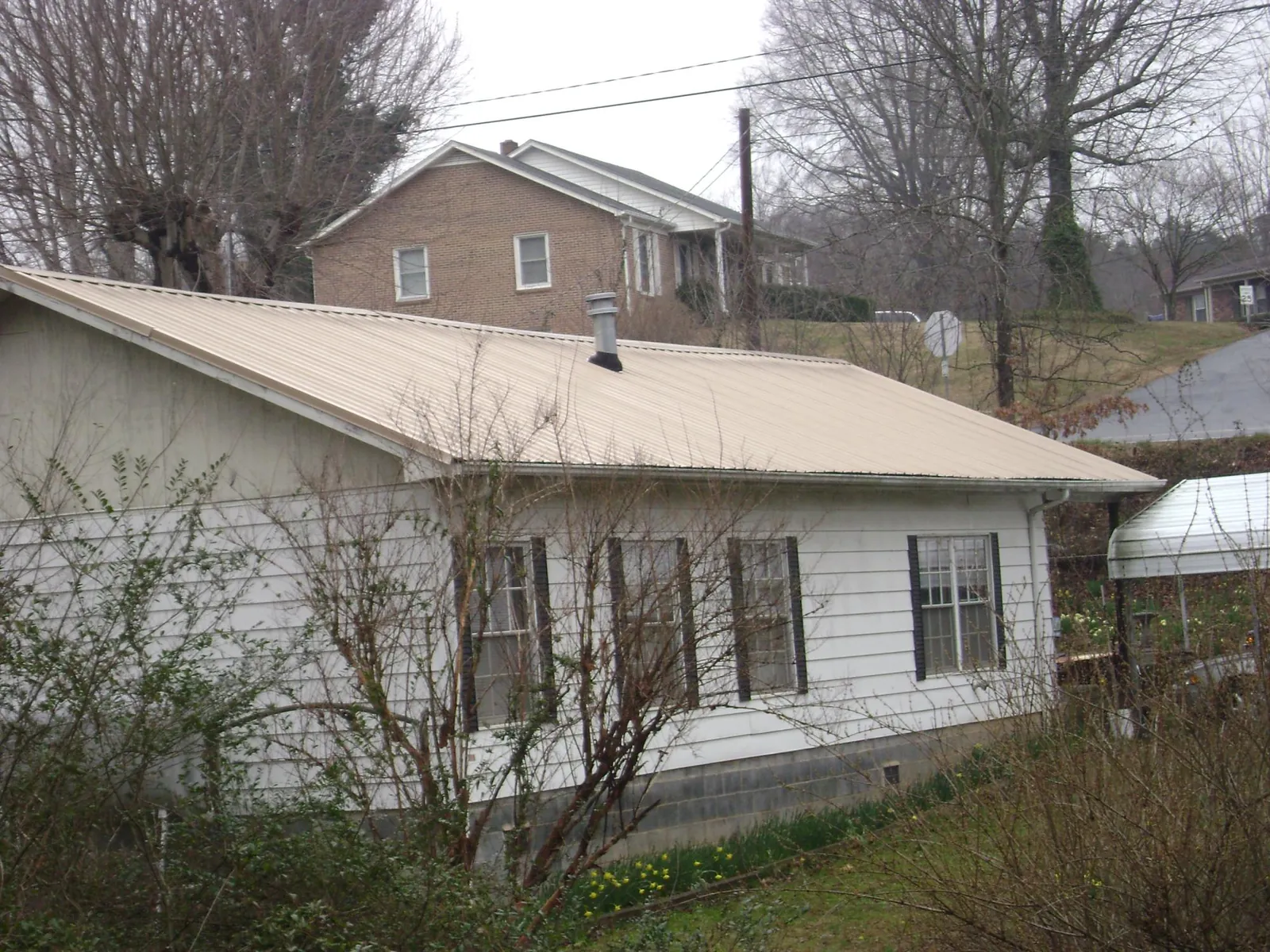 Tan metal roof on a white sided house set into a hillside — Commercial Roofing by Roofing Brothers in Clarksboro